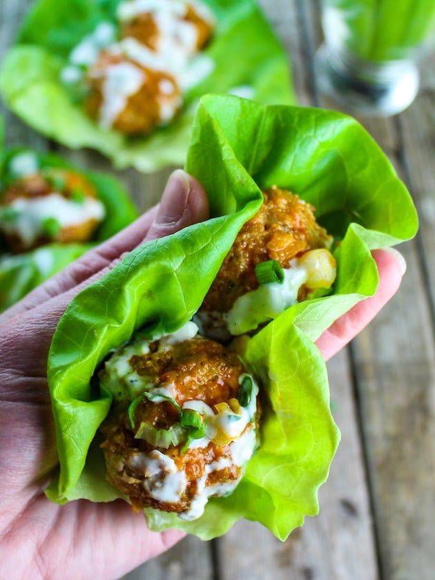 Someone holding two buffalo-flavored meatballs in a lettuce wrap.