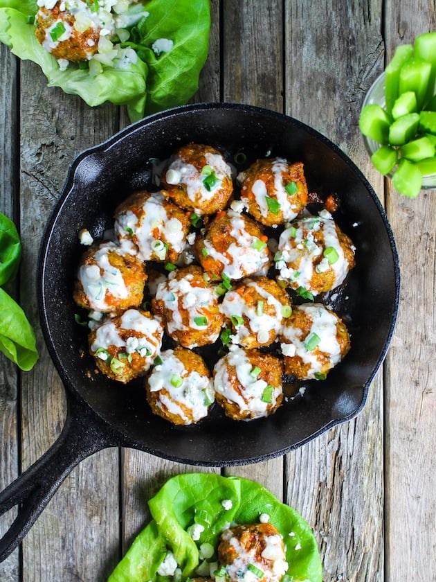 This buffalo chicken meatball recipe is finished in a pan with blue cheese sauce drizzled on top and lettuce wraps.