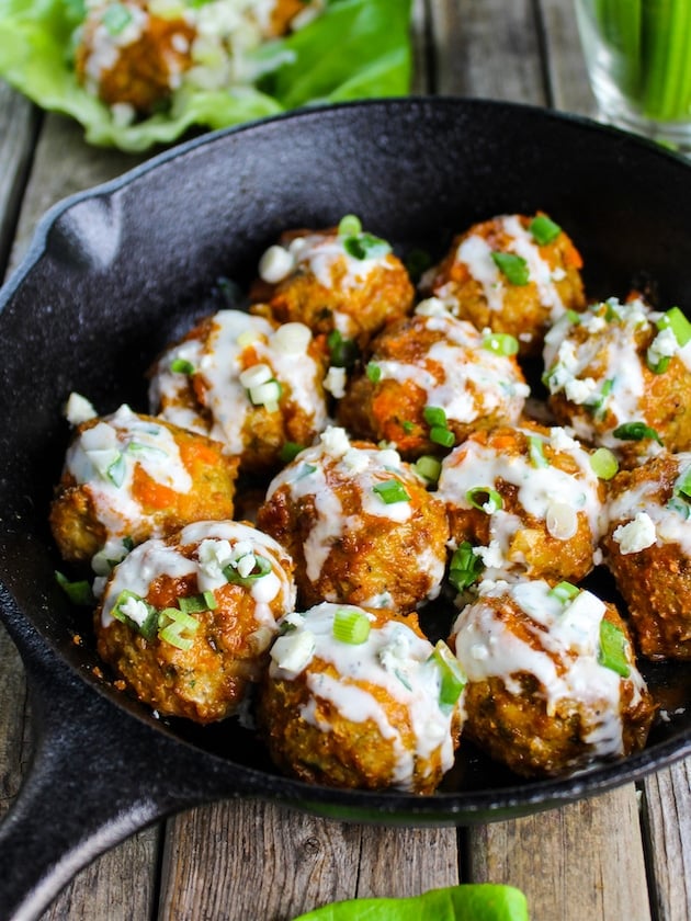 Baked buffalo chicken meatballs in a pan with blue cheese sauce drizzled on top.