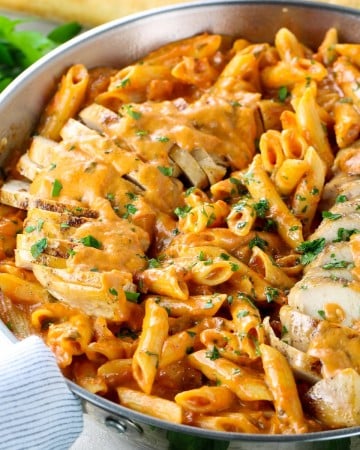 A pan of penne pasta tossed in vodka sauce and topped with sliced grilled chicken.
