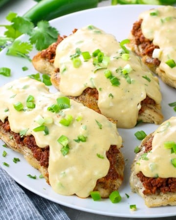 A plate with grilled chicken topped with cooked ground chorizo and topped off with a cheese sauce.