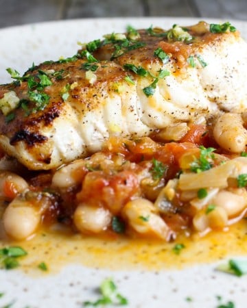 One piece of cooked halibut on a plate with sauteed cannellini beans.