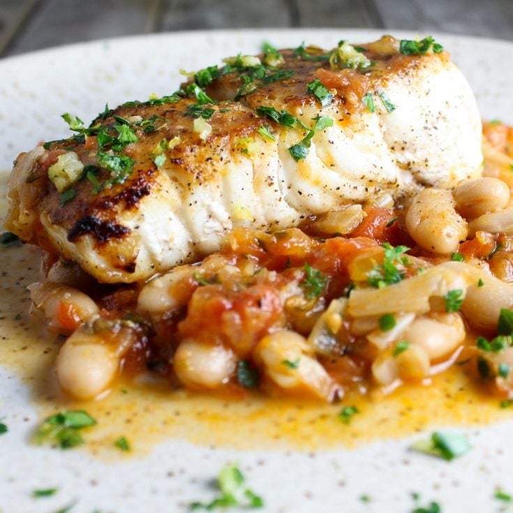 One piece of cooked halibut on a plate with sauteed cannellini beans.