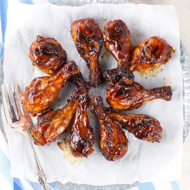 A large plate with grilled chicken drumsticks covered in BBQ sauce.