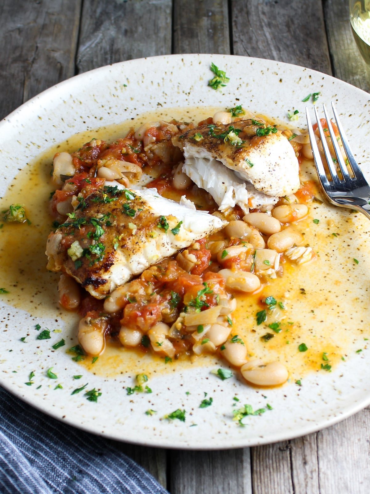 One piece of cooked halibut cut in half on a plate with sautéed cannellini beans.