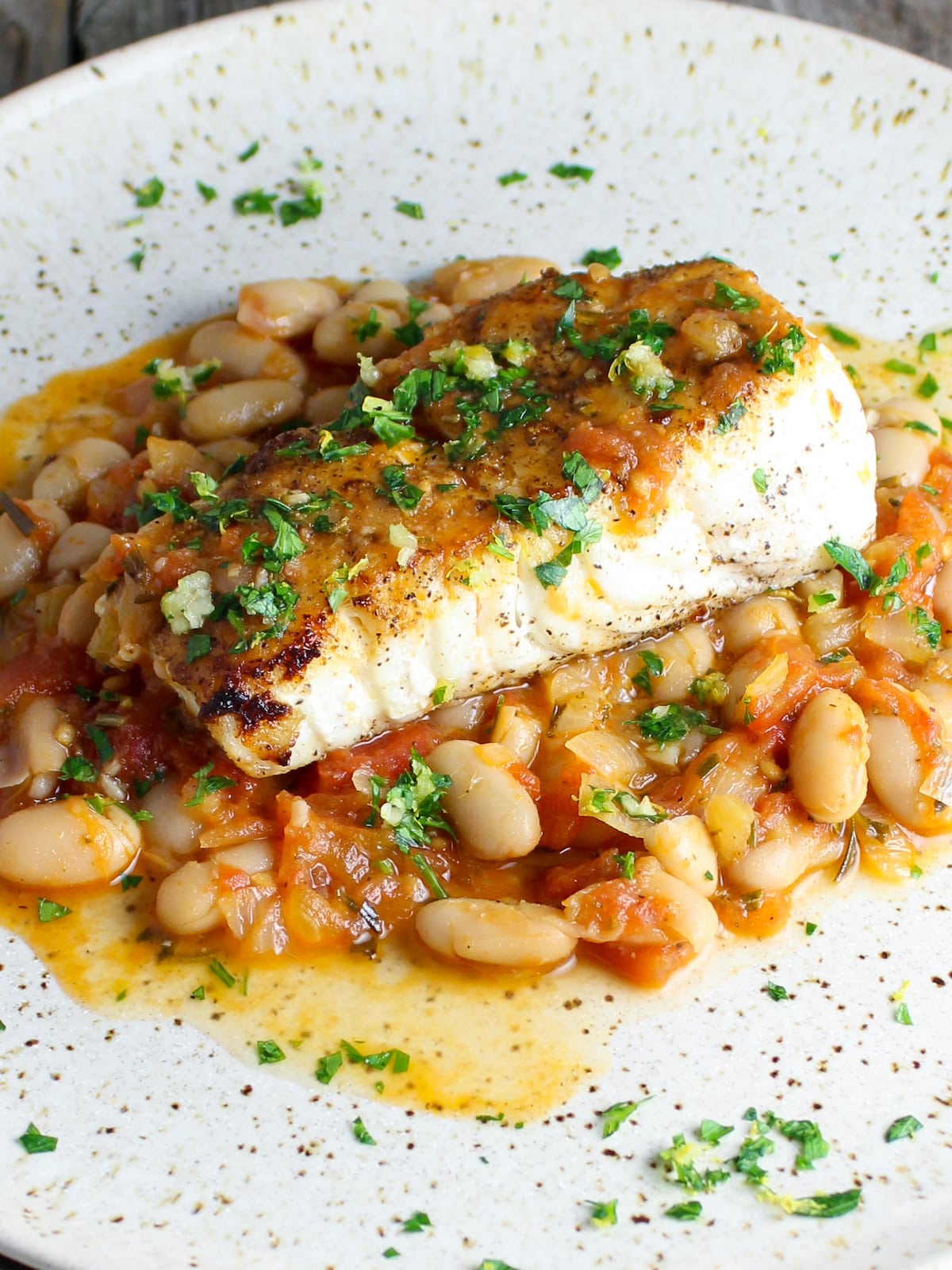One piece of the most delicious white fish on a plate with sautéed tomatoes and cannellini beans.