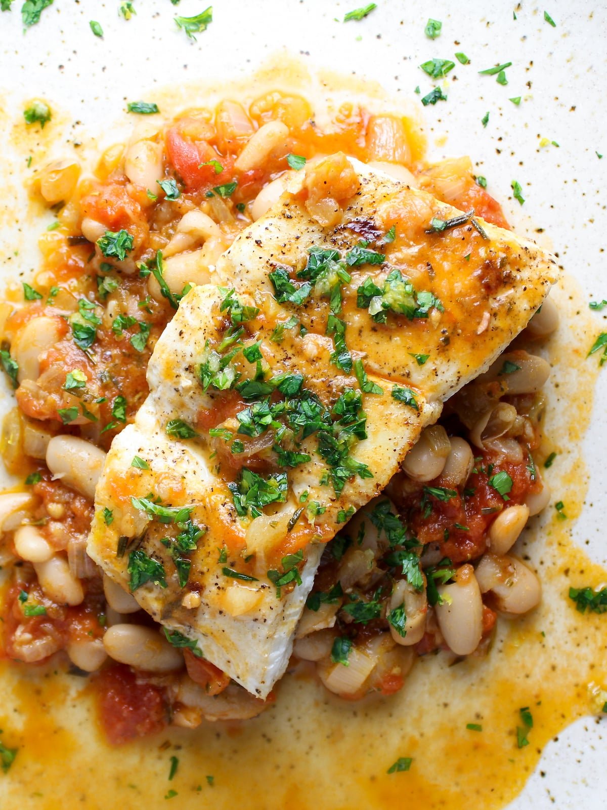 Cooked halibut on a plate with sautéed cannellini beans.