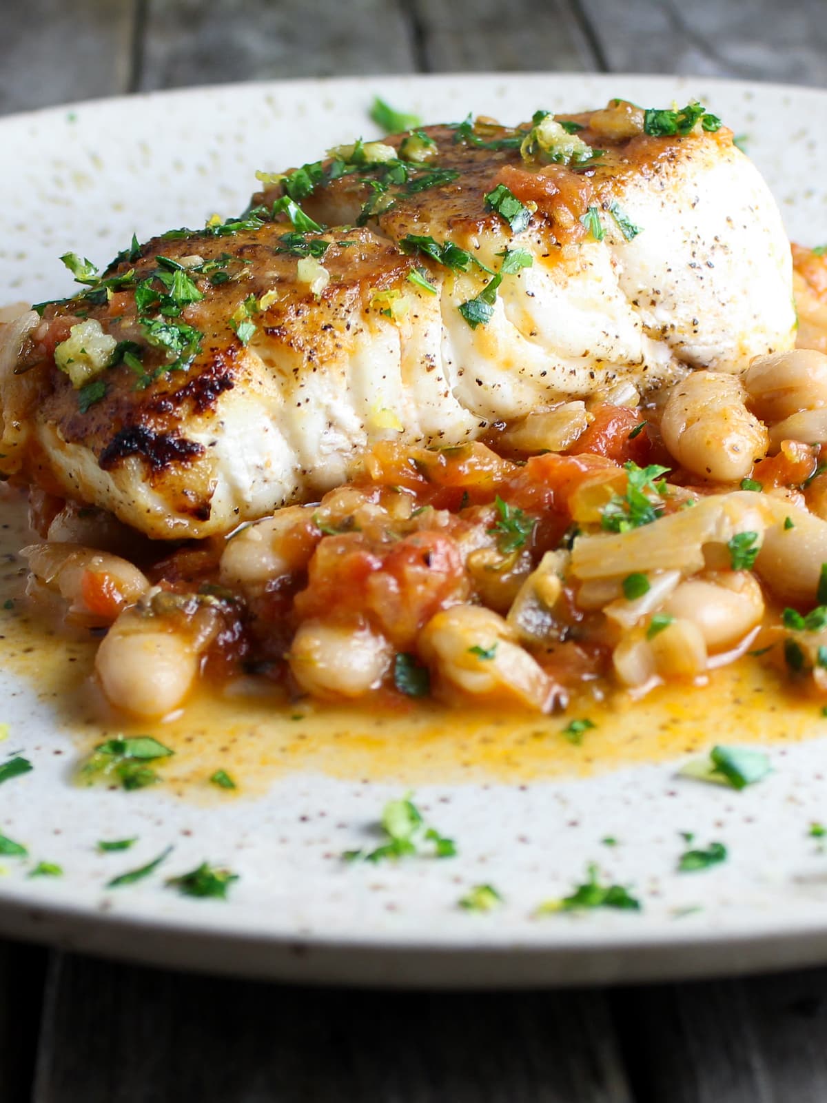 Pan Seared Halibut on a plate with sauteed white beans, chicken broth, and tomatoes.