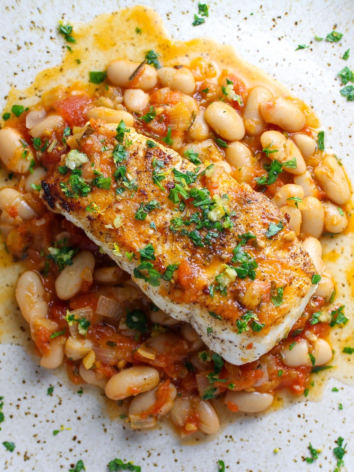 Pan Seared Halibut on a plate with sauteed white beans, chicken broth, and tomatoes.