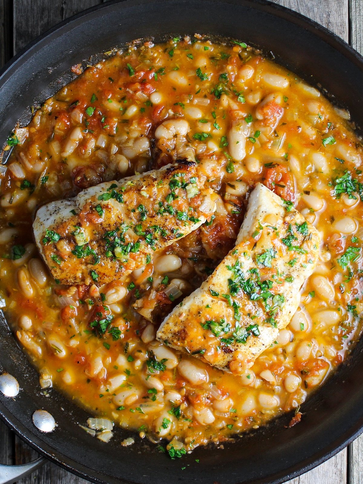 Fish sautéed in a pan with white beans, chicken broth, and tomatoes.