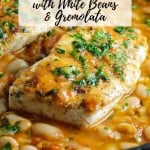 A pan with pan-seared halibut over cauteed white beans, cherry tomatoes and chicken broth.