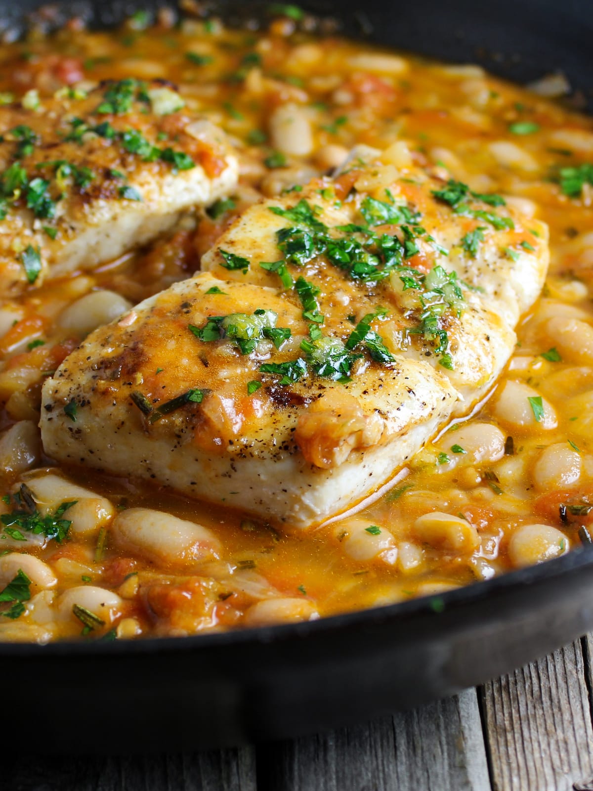 Halibut sauteed in a pan with white beans, chicken broth, and tomatoes.
