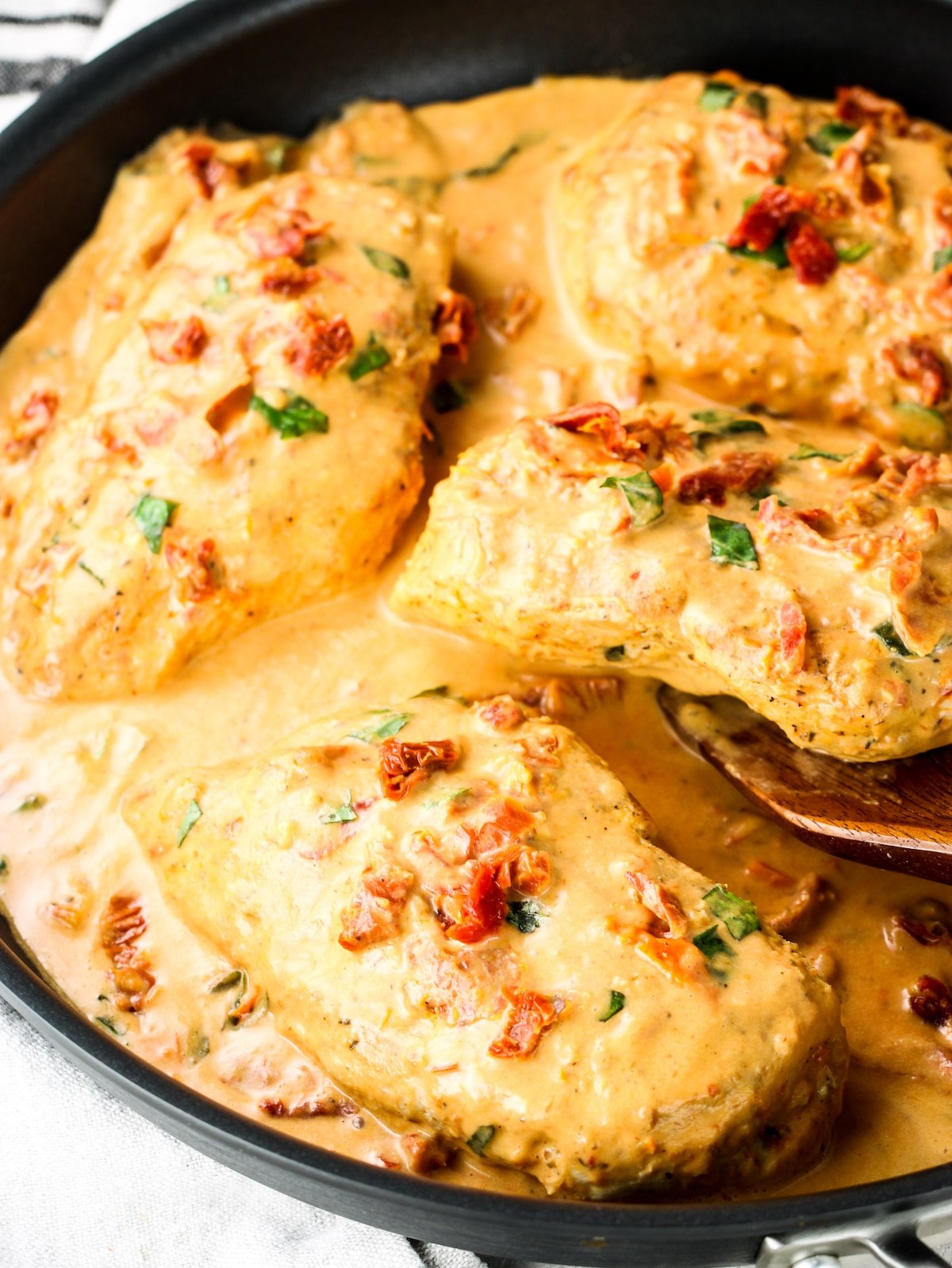 A close-up photo of chicken breasts in a creamy sun-dried tomato sauce.