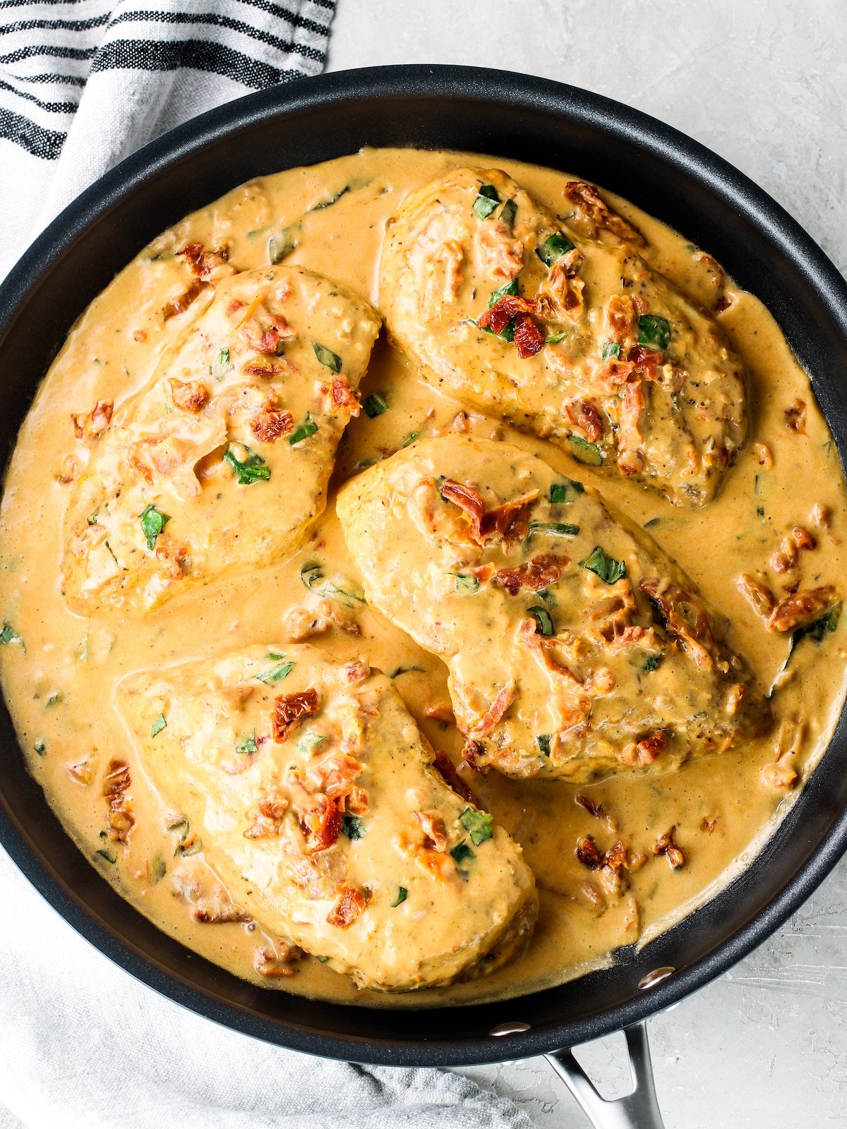 A saucepan with four cooked chicken breasts in a creamy sun-dried tomato sauce.