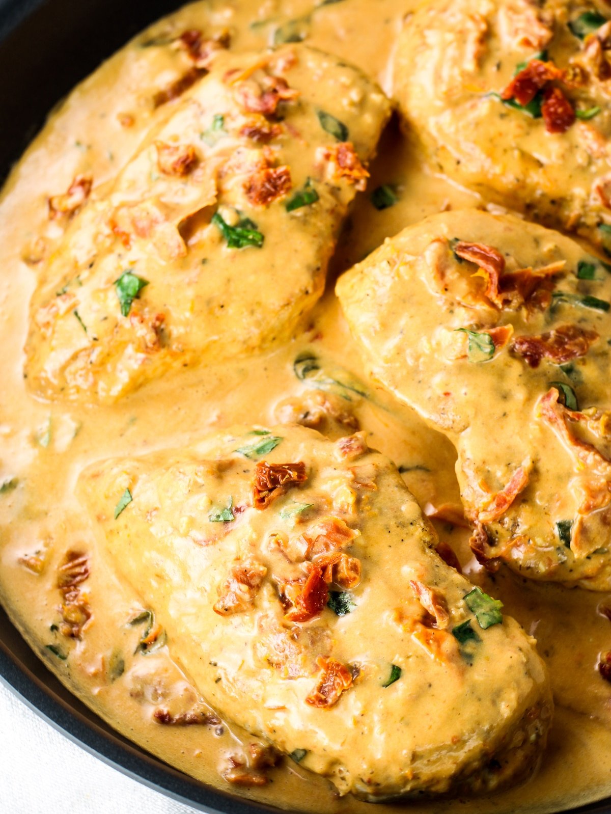 A very close-up photo of a saute pan with cooked chicken breasts in a creamy sun-dried tomato sauce.