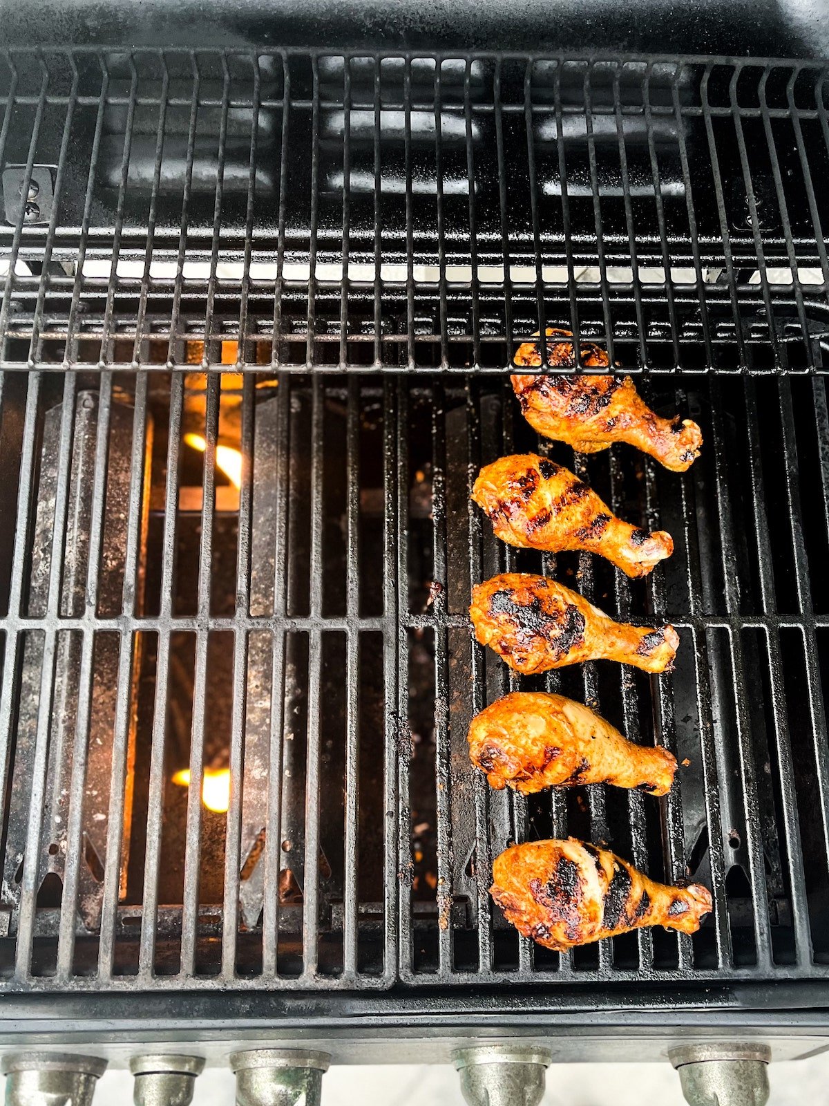 Drumsticks are being grilled on the side of the grill with the burners off.