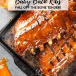 A Pinterest pin for BBQ Baby Back Ribs on a baking sheet with BBQ sauce on the side.