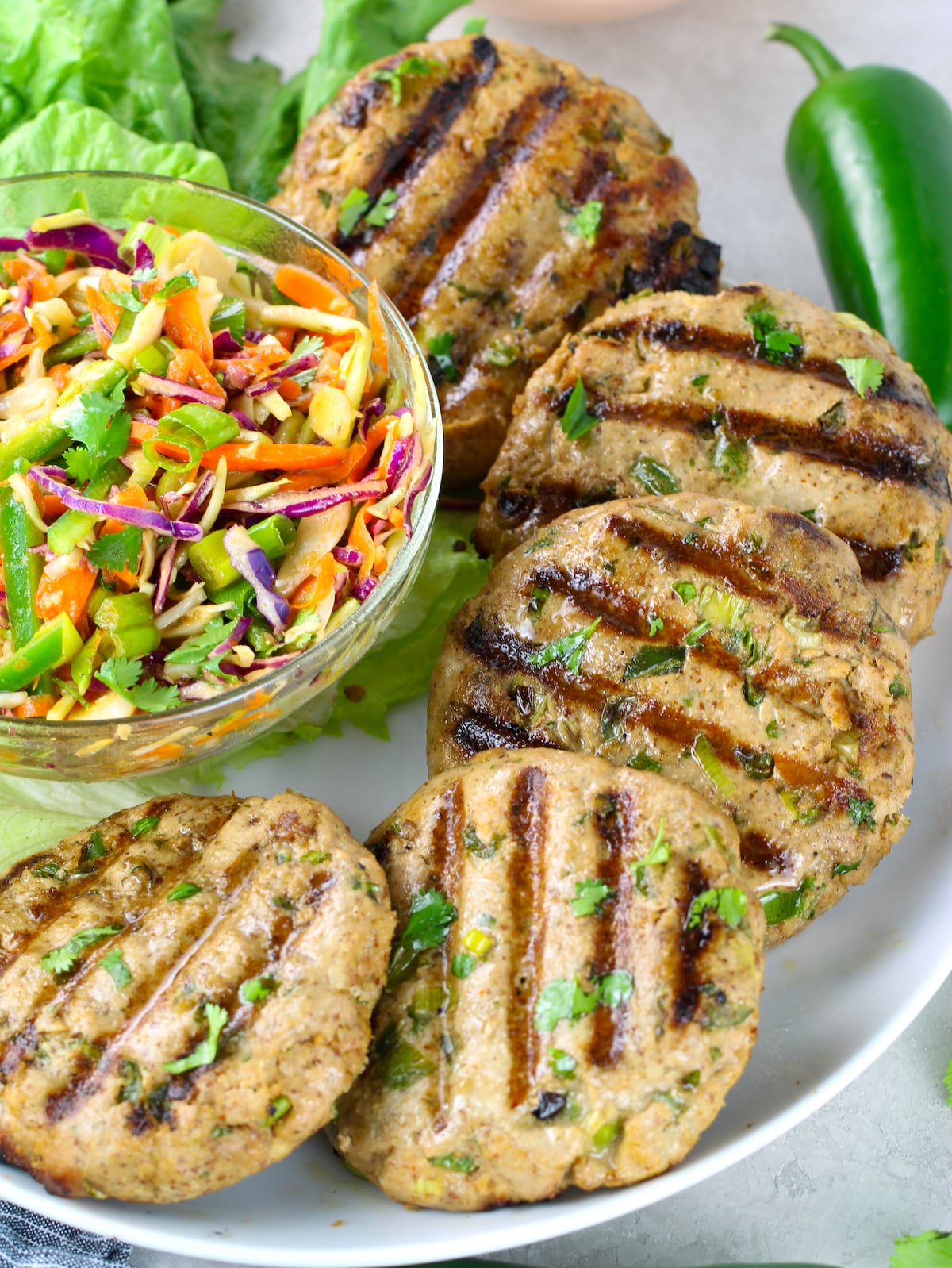 Grilled tuna patties on a platter with a bowl of Asian slaw.