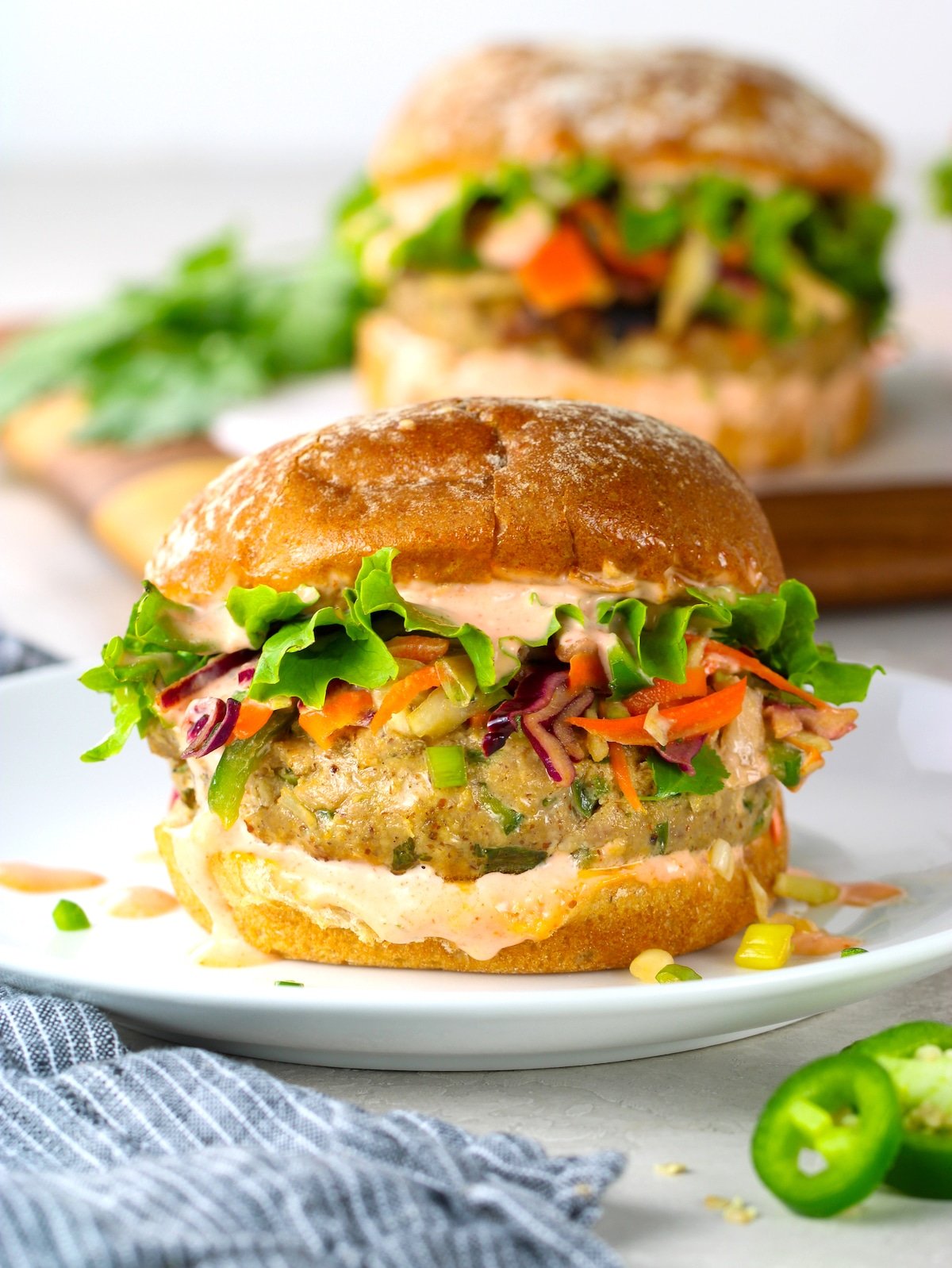 A fish burger with Asian slaw and Sriracha aioli on a plate with more burgers in the background on a serving board.