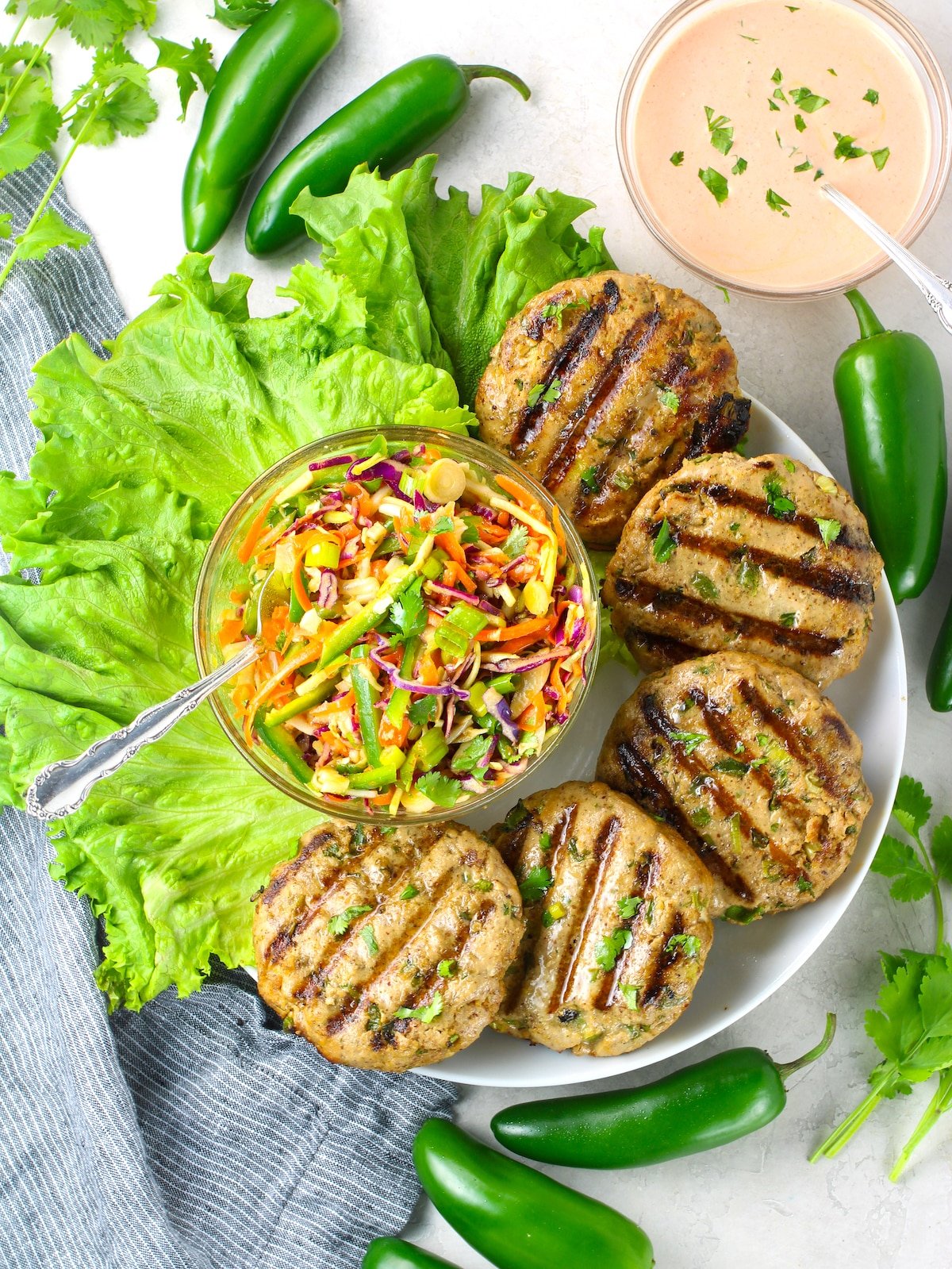 Grilled tuna patties on a platter with a bowl of Asian slaw and Sriracha aioli.