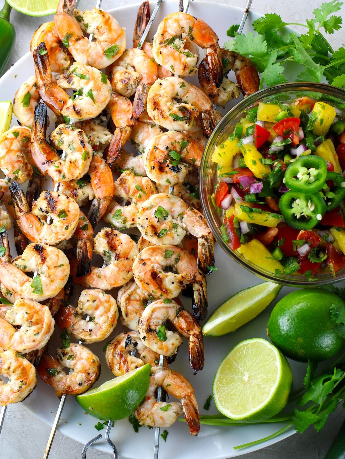 Platter of grilled shrimp on skewers with pineapple salsa and lime, cilantro, jalapeno garnish.