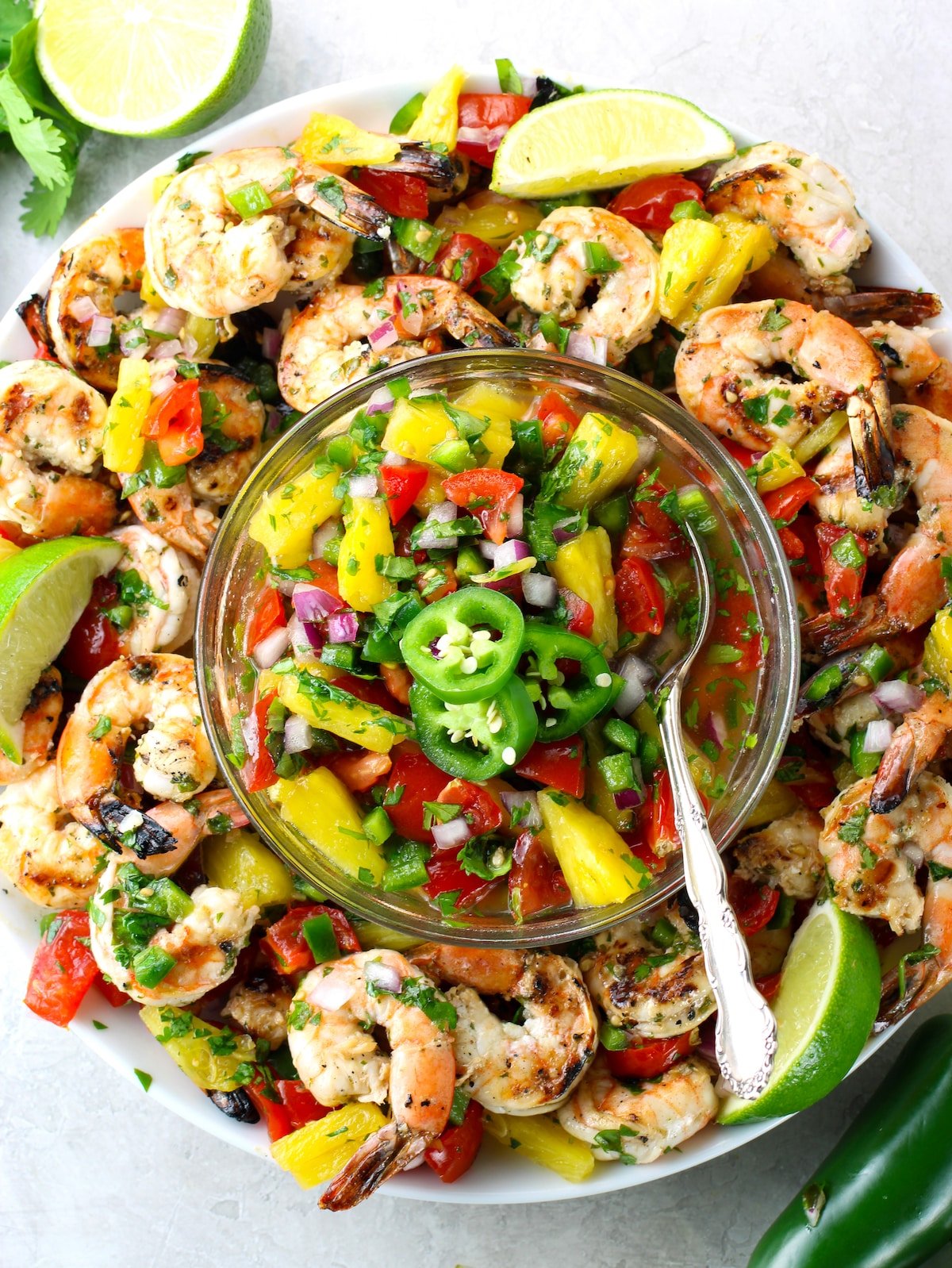 A platter of grilled shrimp with a glass bowl of pineapple salsa in the center.