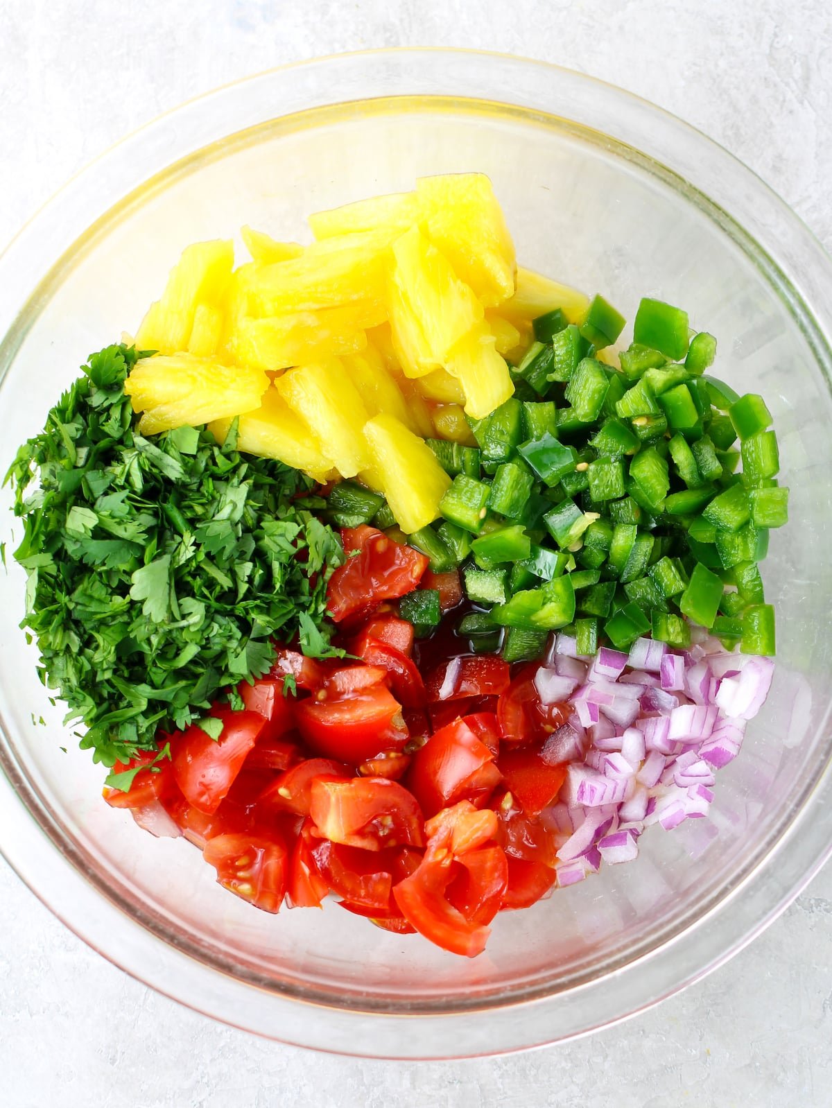 A glass mixing bowl with ingredients for pineapple salsa.