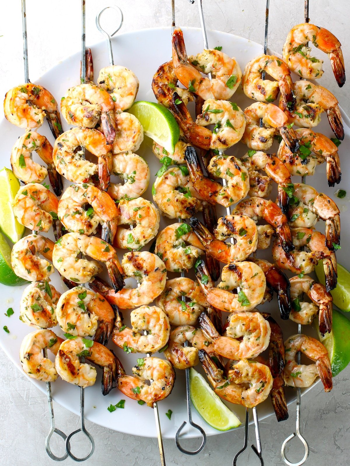 Skewers of grilled shrimp on a platter with lime wedges.