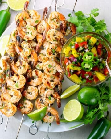 Skewers of grilled shrimp on a platter with pineapple salsa.