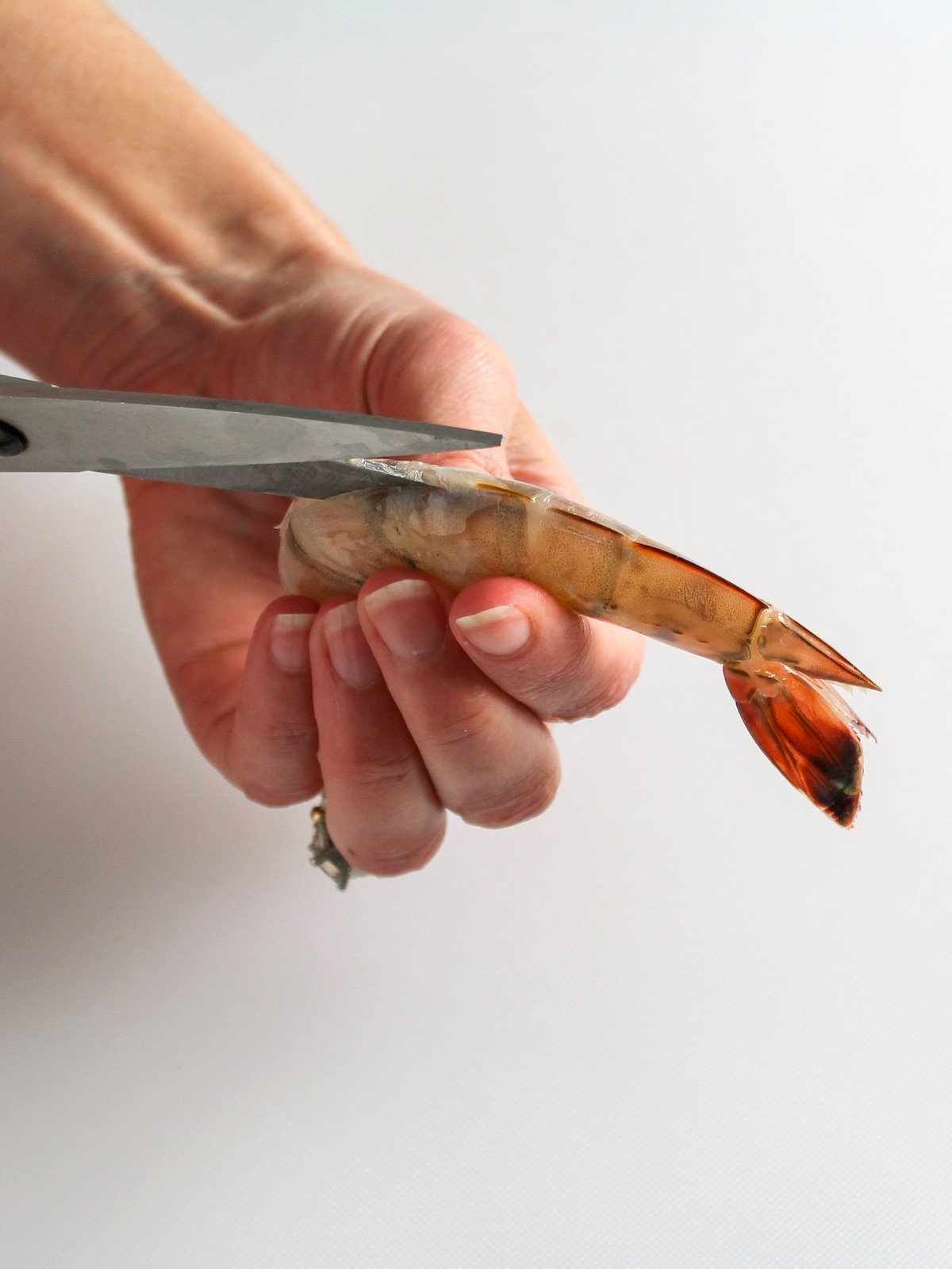 Using kitchen shears to remove the shell from shrimp.