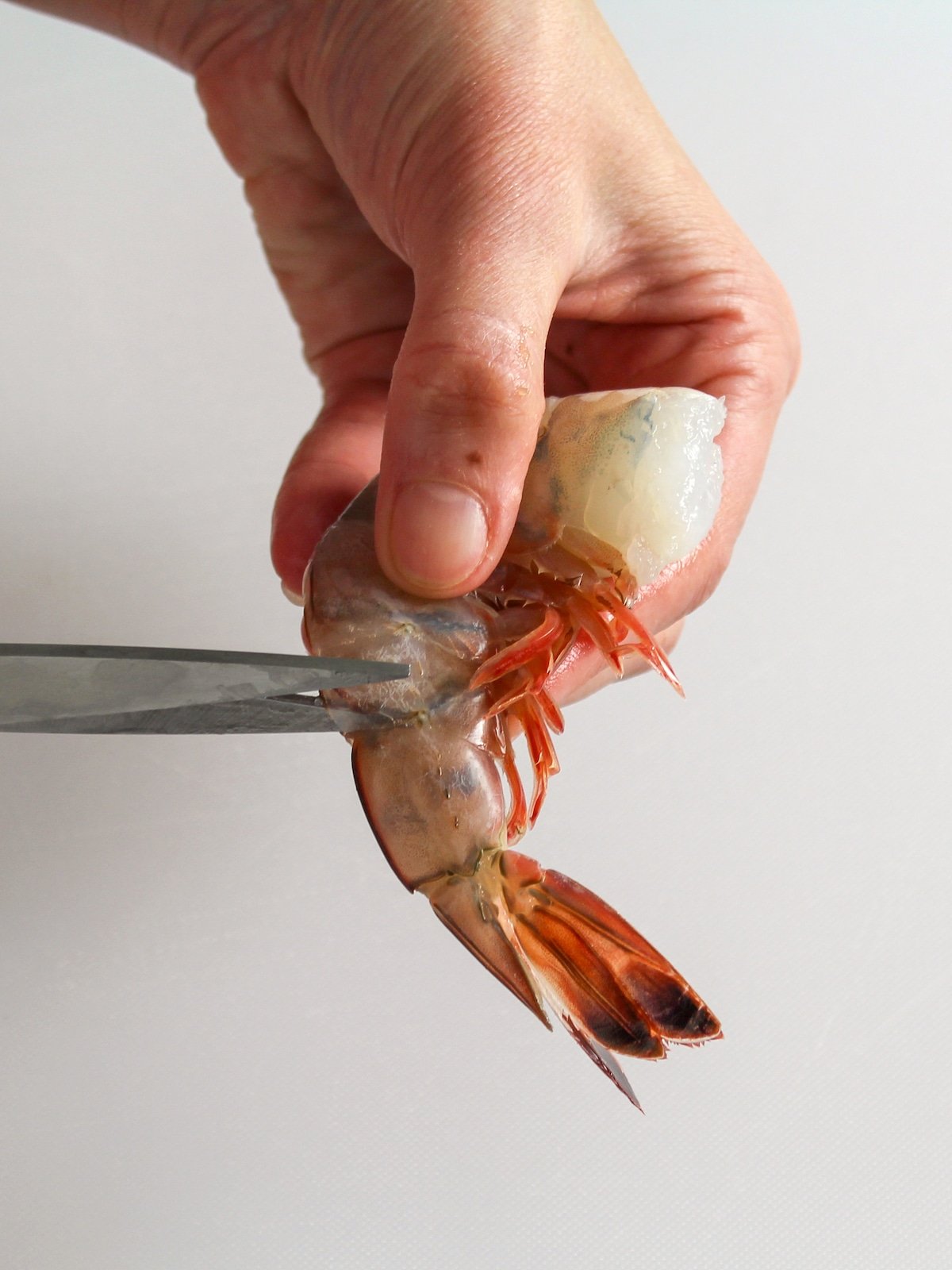 Using kitchen shears to remove the shell from shrimp.