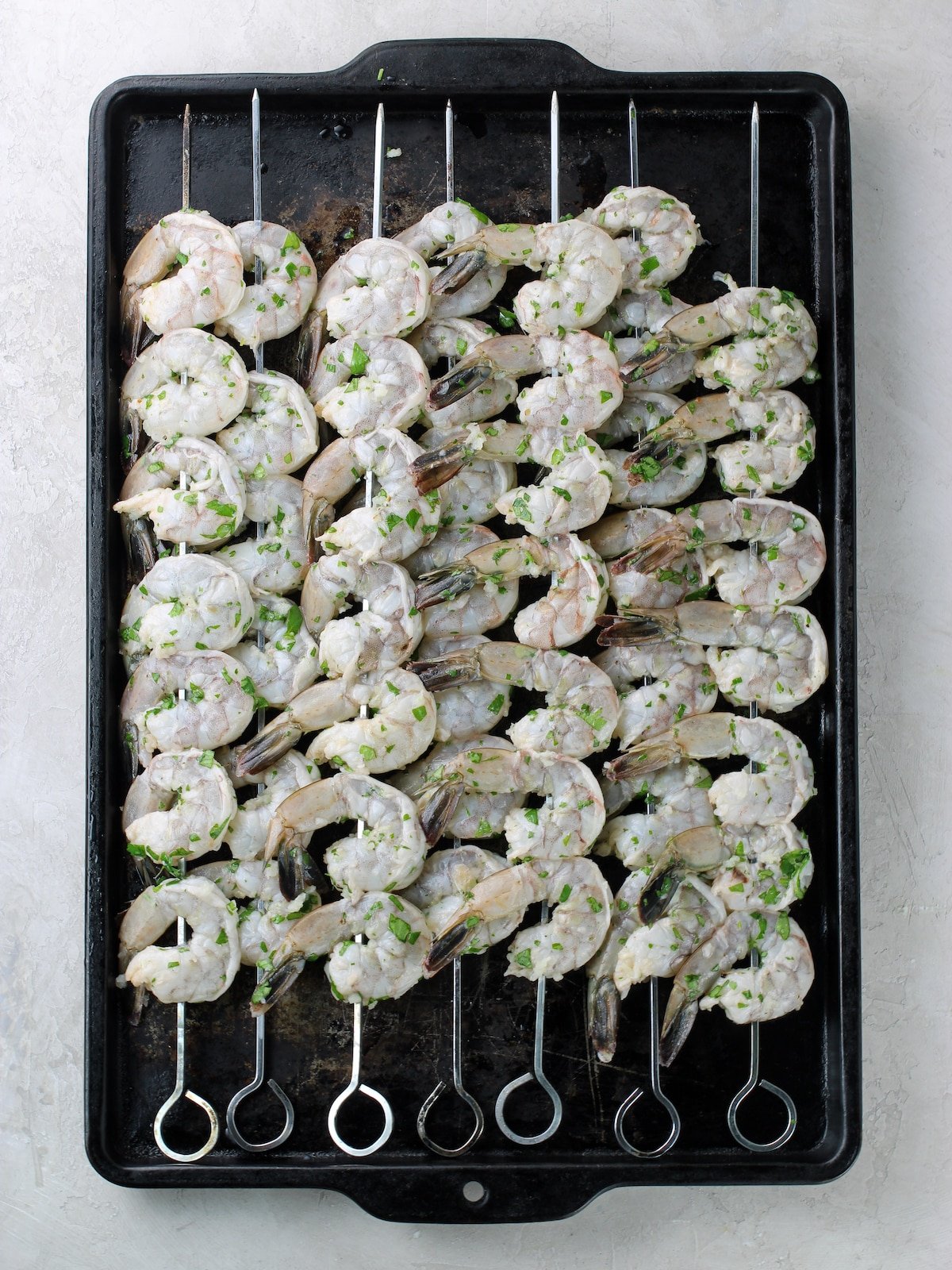 7 skewers of shrimp on a baking sheet ready to grill.