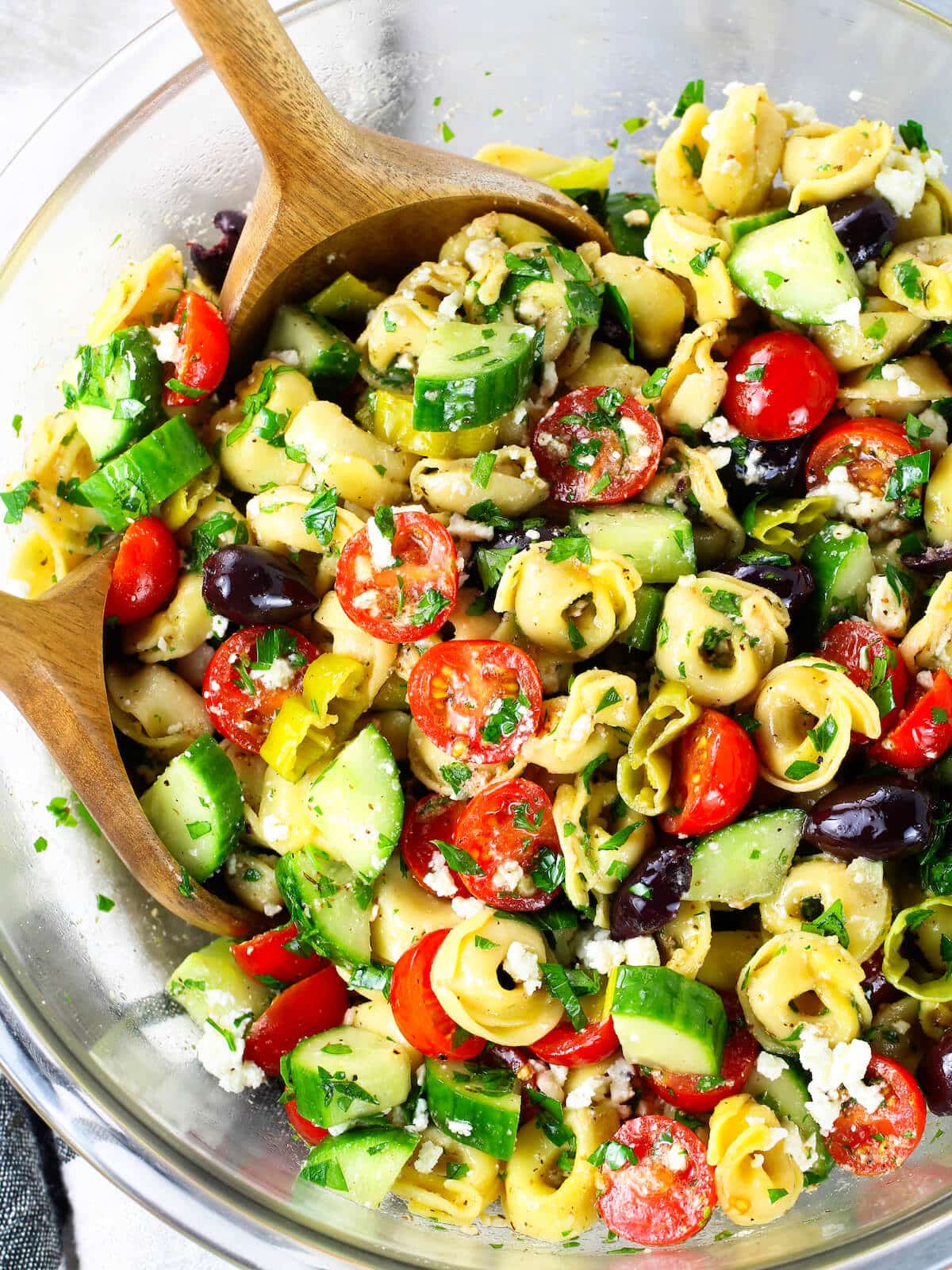 A large half bowl with serving utensils for this salad with pasta, veggies and Greek dressing.