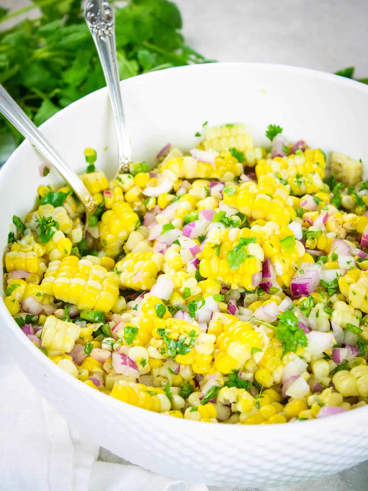 A bowl with a serving spoon full of Jalapeño Cilantro Mexican Corn Salad.