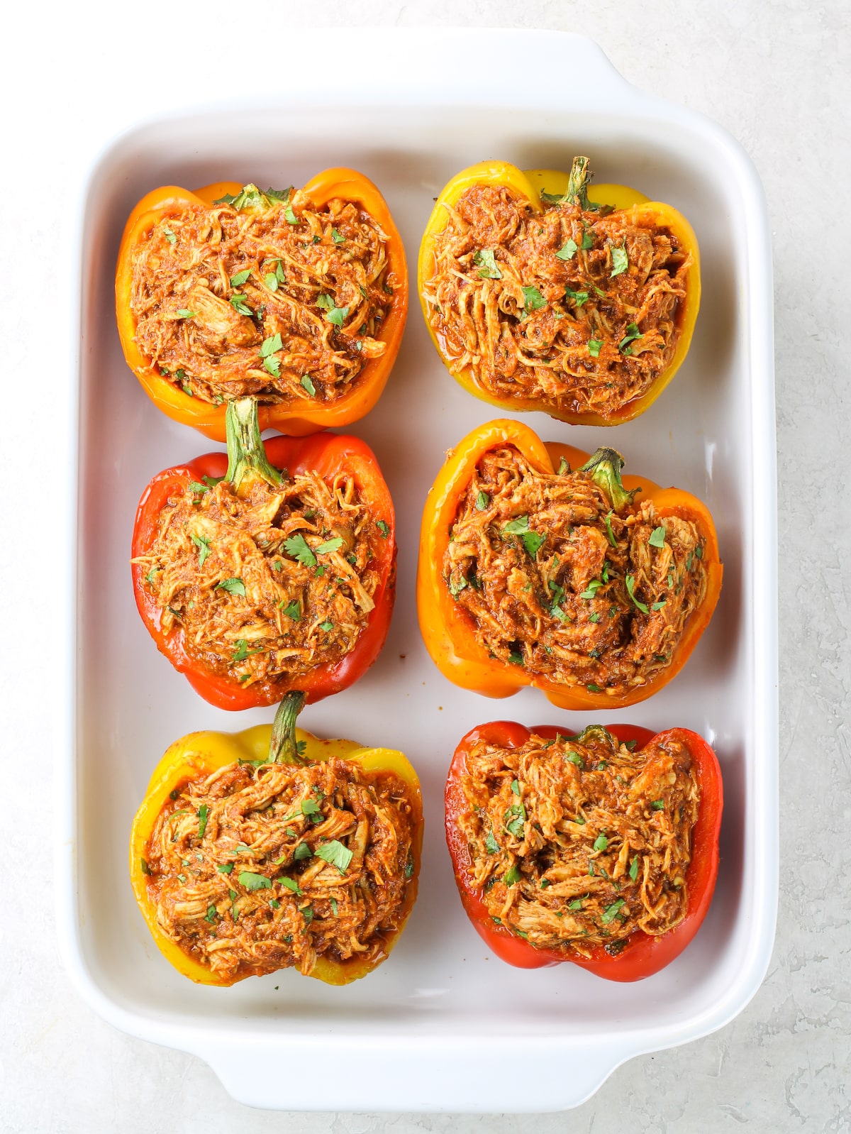 A casserole dish of 6 stuffed peppers with zesty shredded chicken.