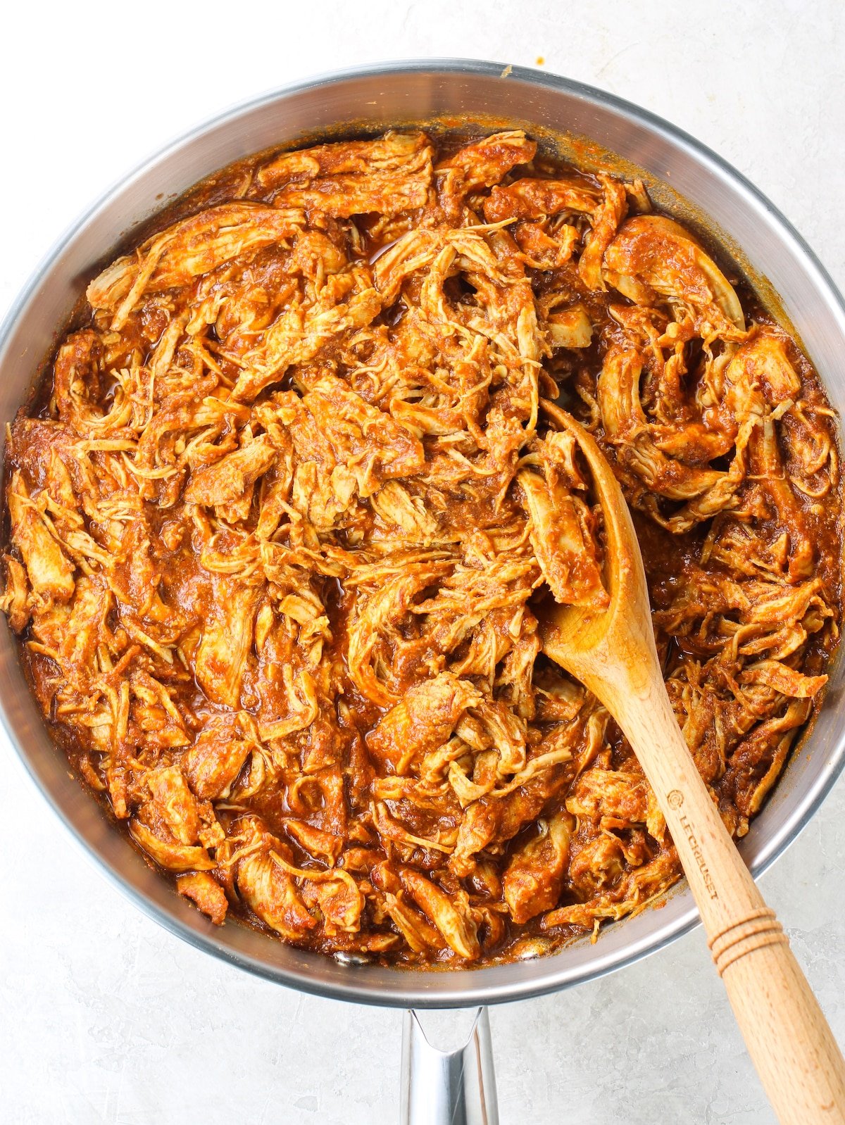 A pan with cooked shredded chicken breasts tossed in a zesty sauce.