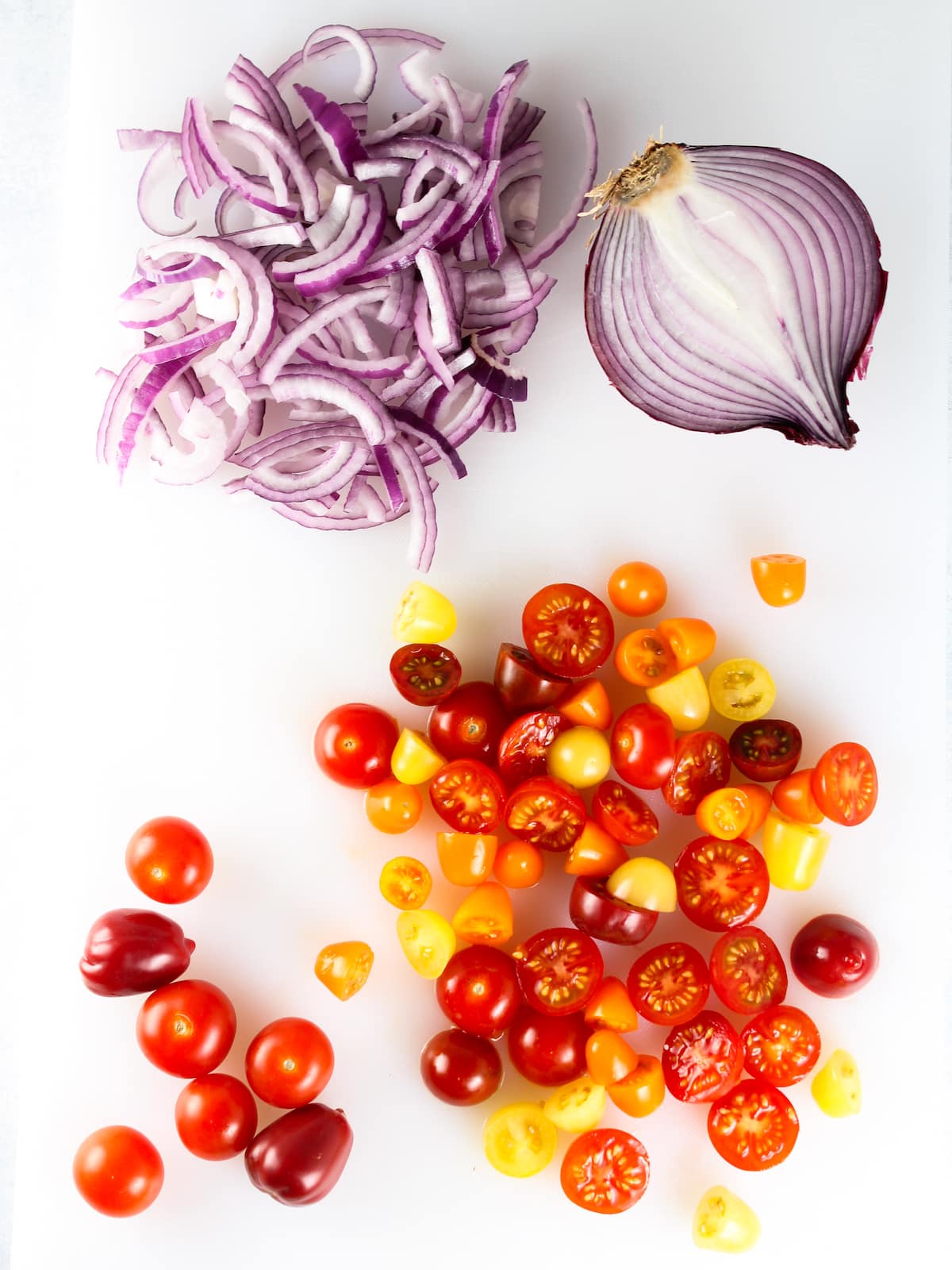 Chopped red onion and sliced tomatoes on a cutting board.