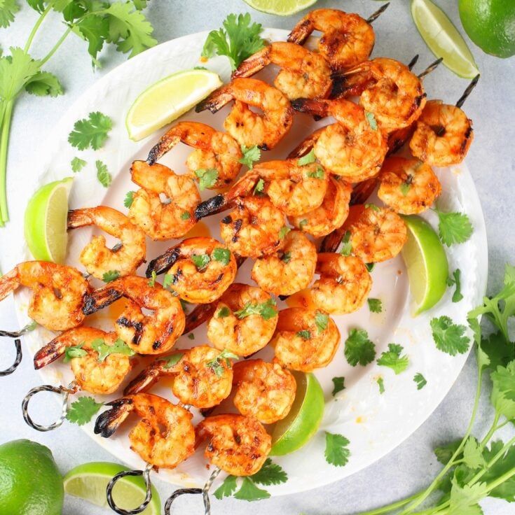 A platter with cooked shrimp on skewers.