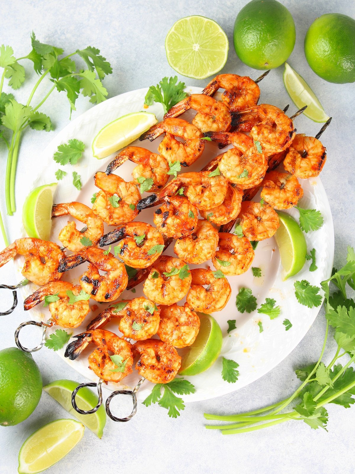 A platter with grilled shrimp on skewers with lime wedges and cilantro.