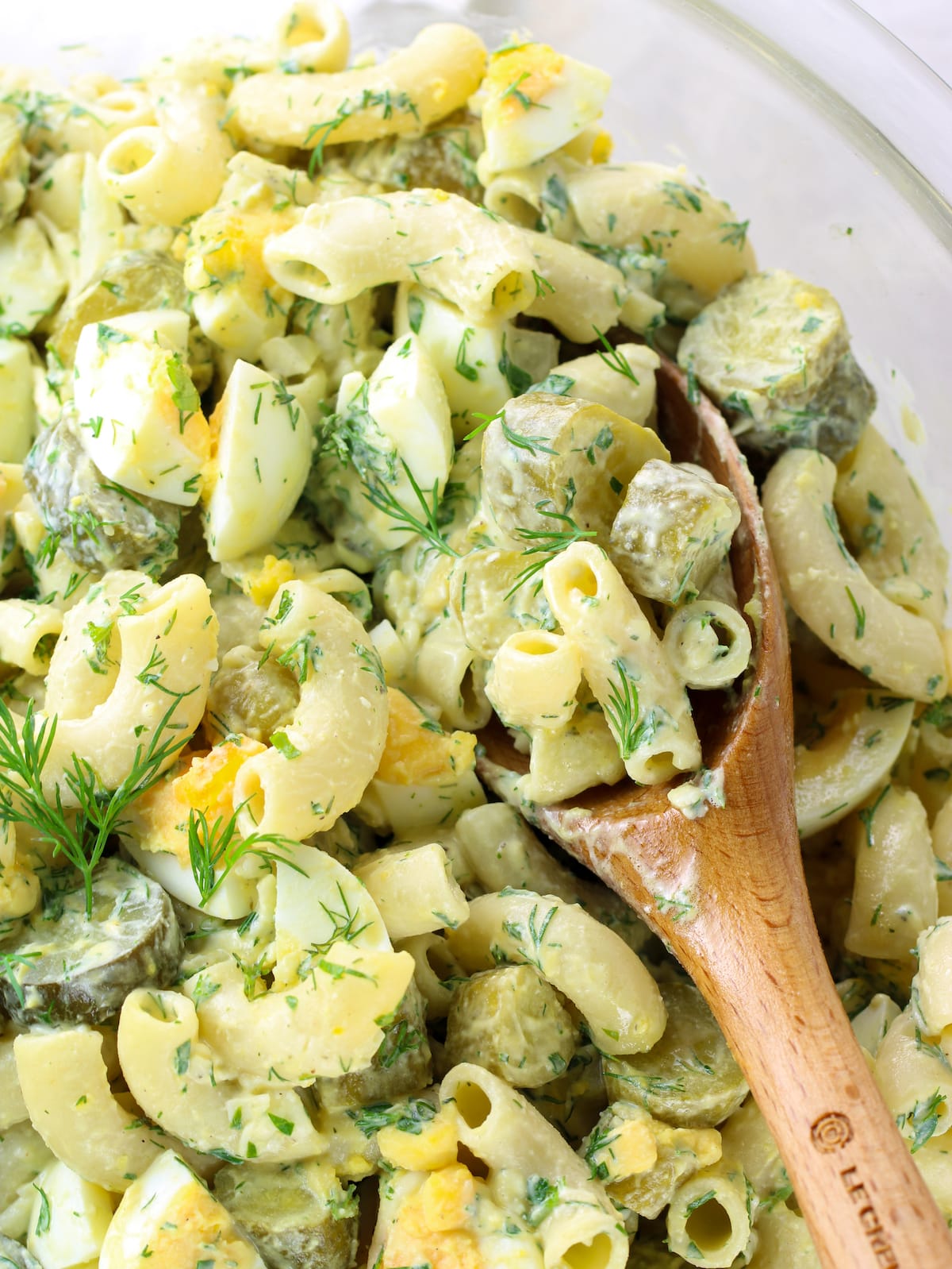 A bowl of Pasta salad with pickles, eggs and seasoning.