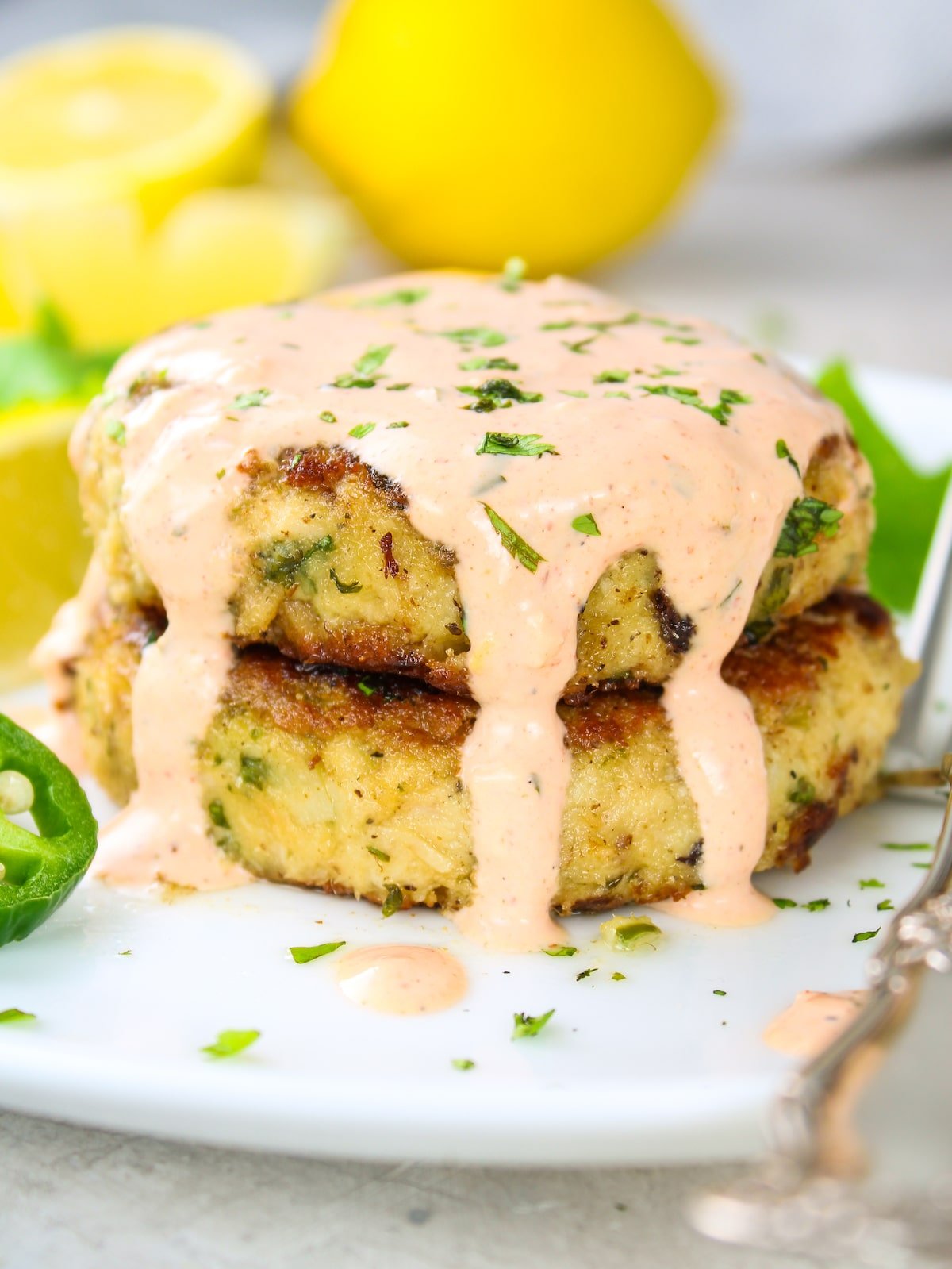 Two tuna cakes on a plate with Sriracha aioli drizzled on top of them.