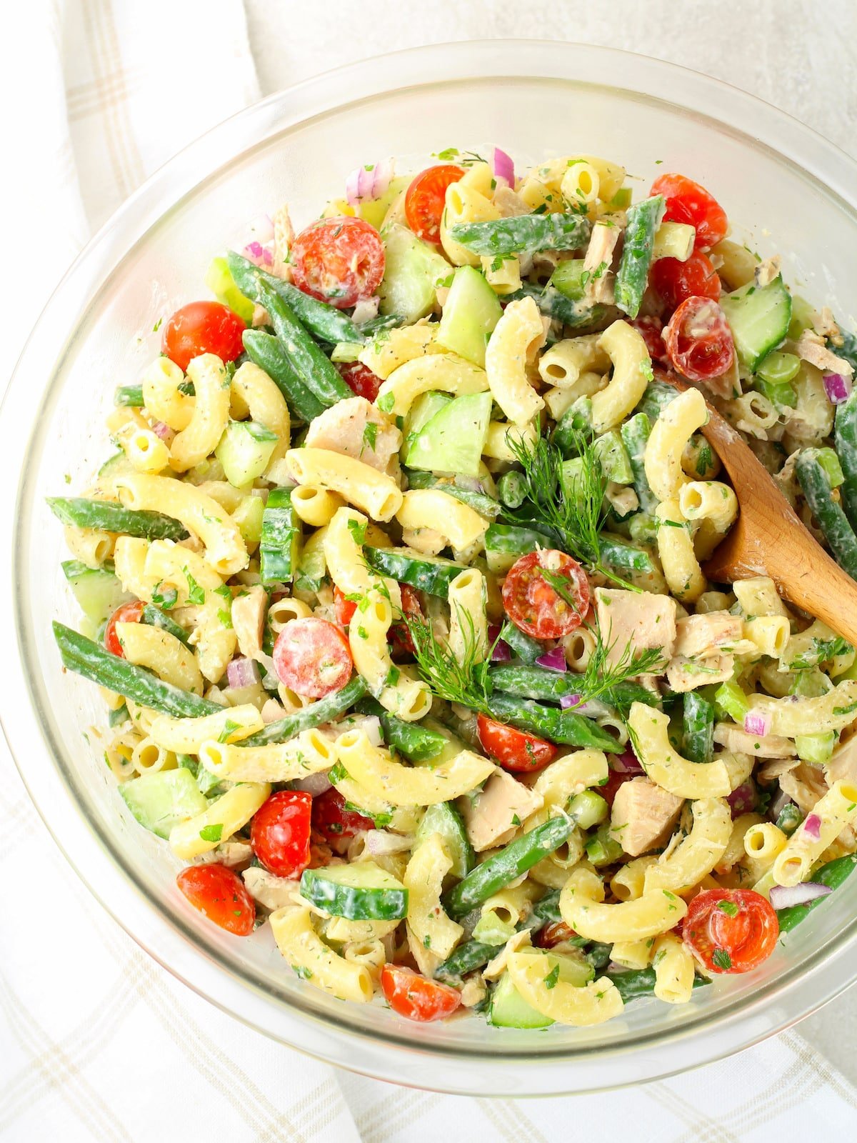 Large glass mixing bowl with pasta, green beans and tomatoes.