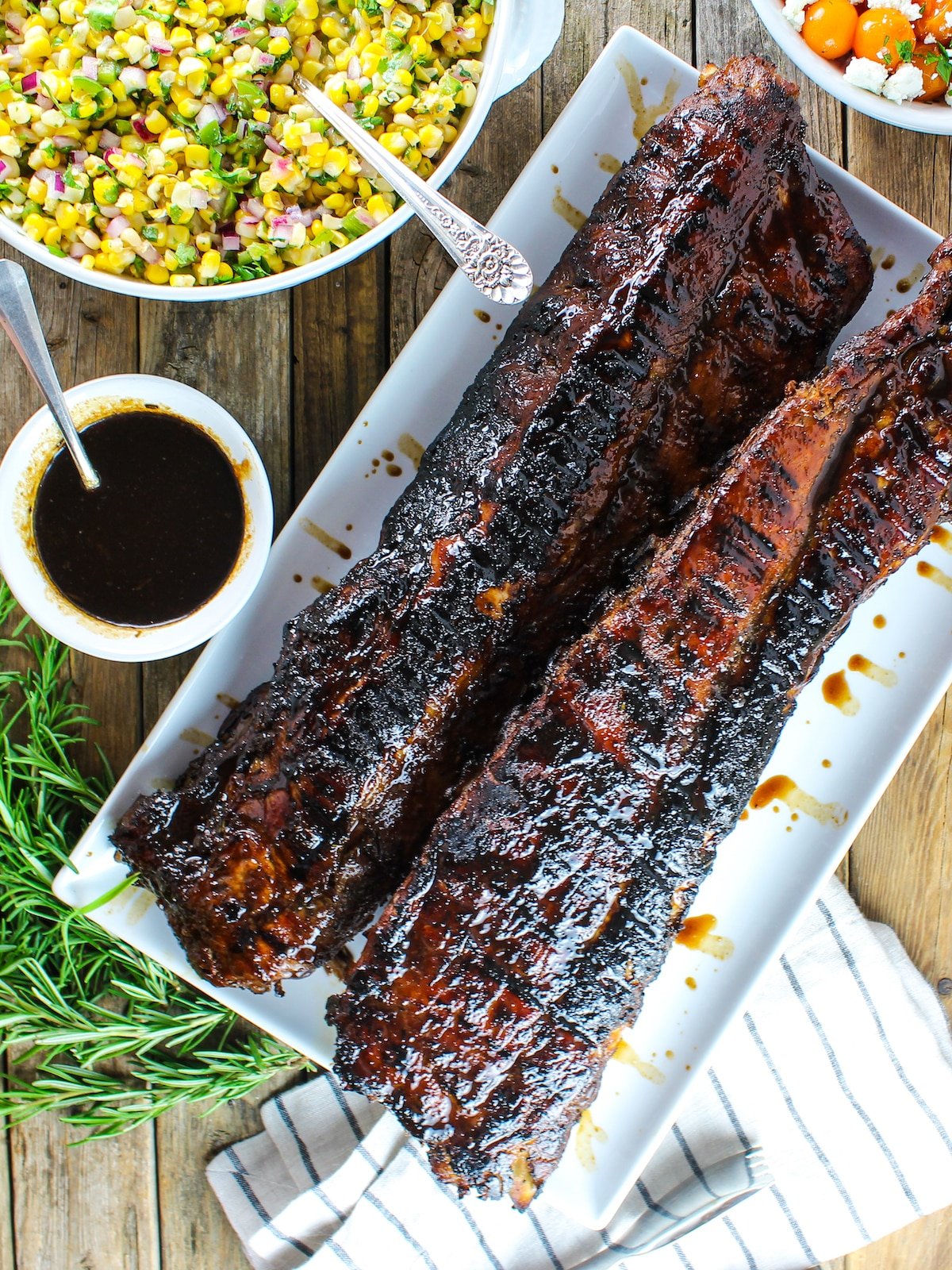 Two racks of glazed sticky Balsamic Baby Back Ribs and corn salad on the side.