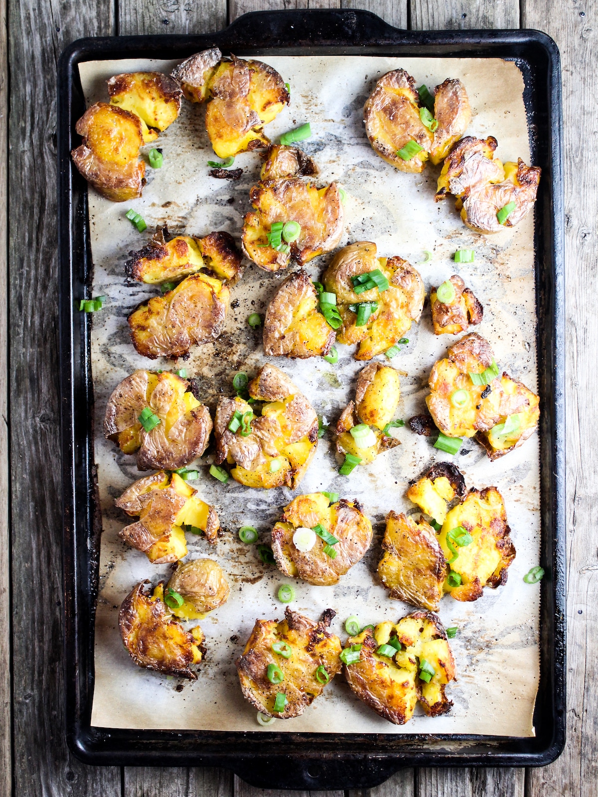 Crispy smashed potatoes on a baking sheet with green onions.