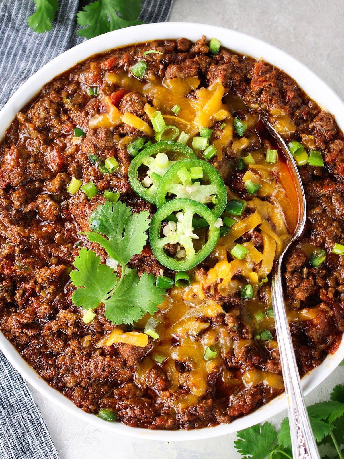A bowl of chili with cheese, jalapeños and green onions.
