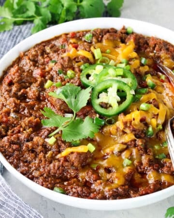 Beef chili in a bowl with cheese, jalapeños and green onions.