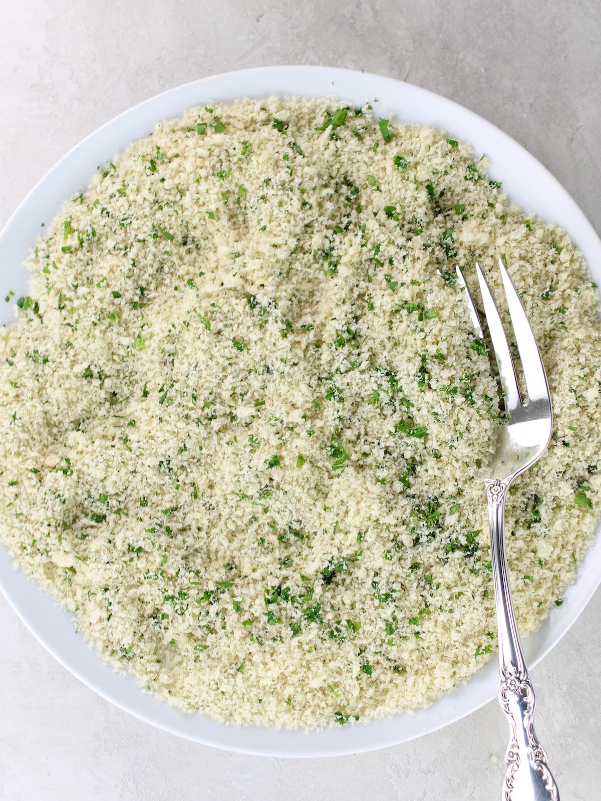 A plate with parmesan cheese, breadcrumbs, parsley, salt and pepper mixed together.