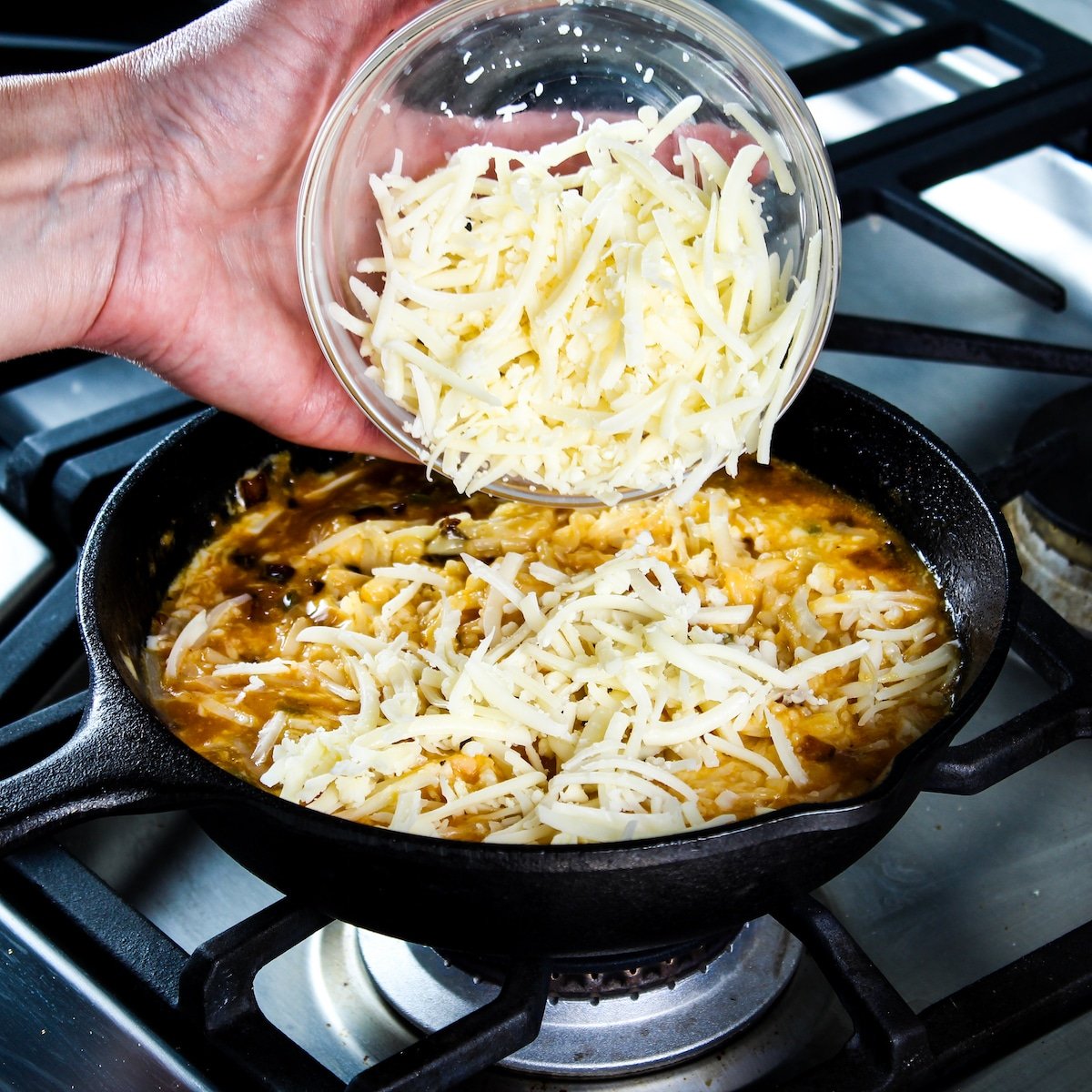 Adding shredded cheddar cheese to the pan of ingredients.