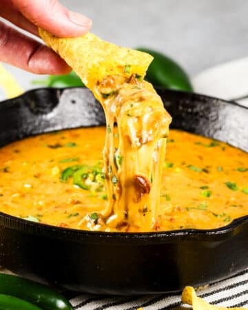 Closeup chip dipping into skillet of Queso Fundido.