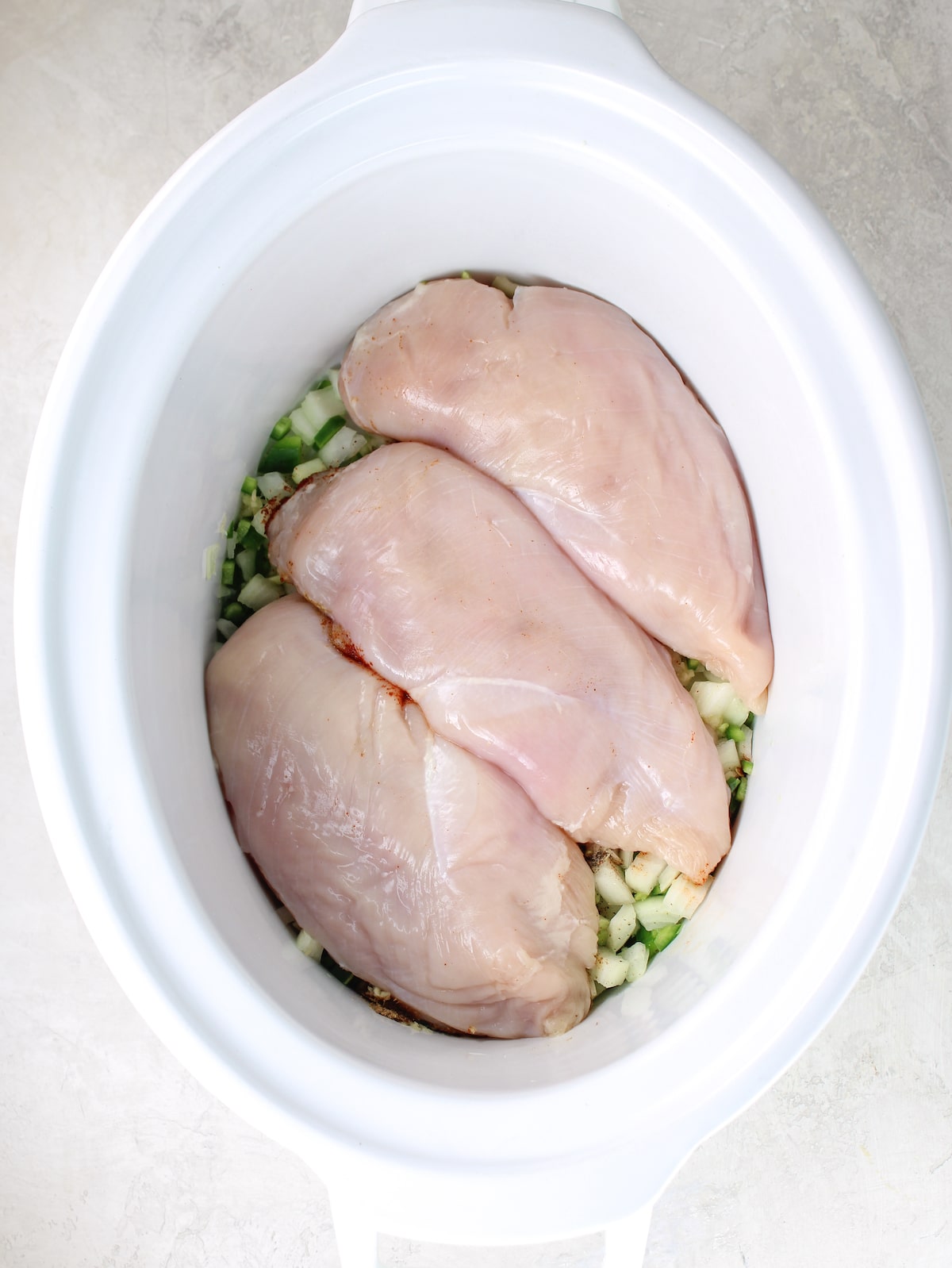 A slow cooker with onion mixture, spices, and raw chicken.
